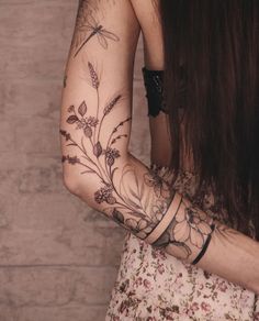 a woman's arm with flowers and dragonflies tattooed on her left arm, next to a brick wall