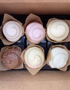 six different types of cupcakes in brown paper wrappers on a black tray