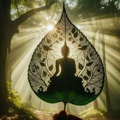 a person holding up a leaf with a buddha statue on it in the middle of a forest