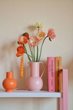 a shelf with books, vase and flowers on it