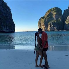 two people are kissing on the beach with mountains in the background