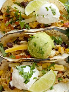 three tacos on a plate with limes and sour cream in the top one