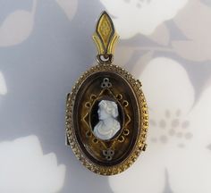 "A carved hardstone cameo is centered on this antique ca. 1880s gold filled locket pendant. The cameo was carved from one black and white stone. The woman is facing left with tiny features, ornate curls and draped clothing. Raised geometric elements with textured detailing frame the cameo. A decorative trim flows around the oval face. The top is fitted with a fancy bail. The locket opens with two pull tabs on the side. Inside are two tin types of a man and woman (who could resemble the cameo). T Victorian Jewelry With Antique Finish Oval Pendant, Victorian Cameo Jewelry For Memorial, Victorian Cameo Jewelry For Memorials, Victorian Cabochon Jewelry For Memorial, Victorian Carved Jewelry For Gifts, Victorian Carved Jewelry Gift, Victorian Jewelry With Antique Finish, Victorian Jewelry With Cabochon Medallion, Antique Finish Jewelry For Memorial