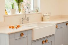 a white kitchen with two sinks and some plants in the window sill next to it