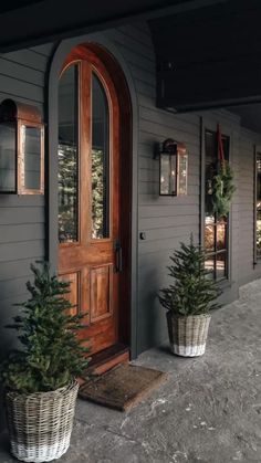 two potted christmas trees sitting on the front porch of a house with wooden doors