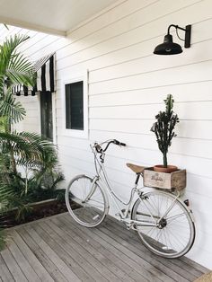 a white bicycle parked on the side of a house next to a potted plant