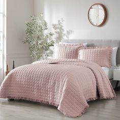 a bed with pink comforter and pillows in a room next to a clock on the wall