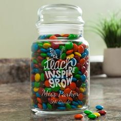 a glass jar filled with lots of colorful candies next to a potted plant