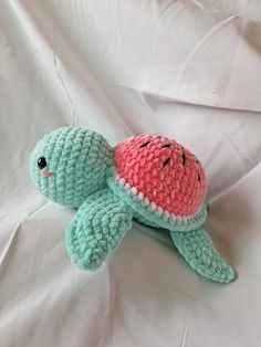 a crocheted stuffed turtle laying on top of a white bed sheet with watermelon in its shell