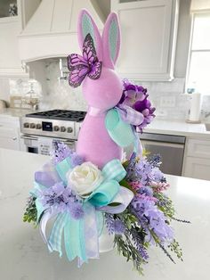 a pink bunny sitting on top of a counter next to purple and white flowers in a vase