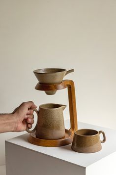 a person is holding a coffee pot and two cups on a stand with a wooden handle