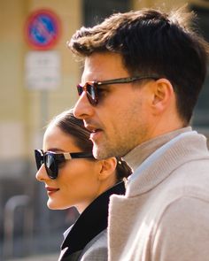 a man and woman are walking down the street together, looking at something in the distance