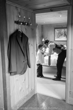 a man standing next to a little boy in front of a suit hanging on a wall