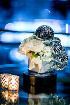 a table topped with a vase filled with white flowers and disco ball decorations on top of it