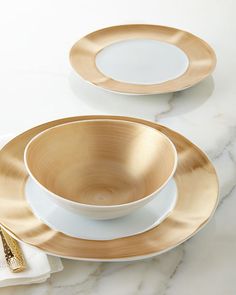 two white and gold plates on a marble countertop with silverware next to them