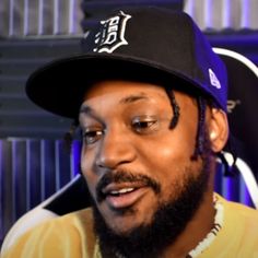 a man with a beard wearing a baseball cap and looking at the camera while sitting down