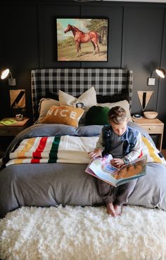 a young boy sitting on top of a bed reading a book in front of him