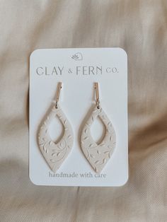 the clay earrings are white and have gold hooks on each earring, with an intricate design