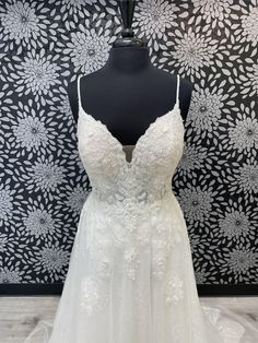 a white wedding dress on a mannequin in front of a floral wallpaper