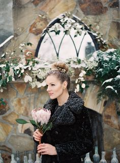 a woman standing in front of a stone wall holding a flower