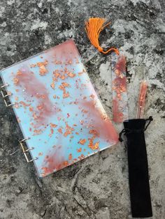 an orange and blue notebook sitting on top of a granite floor next to a black bag