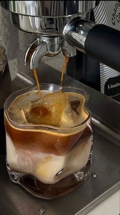 coffee being poured into a glass cup with ice and caramel on the rim, in front of a machine