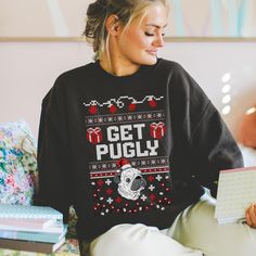 a woman sitting at a table with a laptop wearing an ugly sweater that says get pugly on it