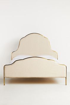 a bed with white linen and gold trim on the headboard, sitting against a wall