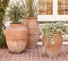 three large vases sitting on top of a brick floor