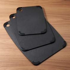 three black cutting boards sitting on top of a wooden table