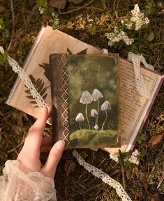 a person holding an open book in their hand while laying on the ground with flowers