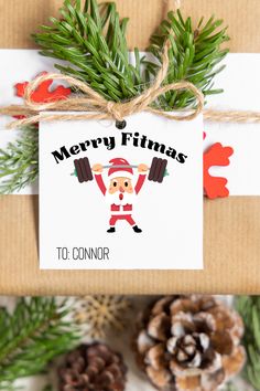 a christmas present wrapped in brown paper next to pine cones and evergreen branches with the words merry fitness on it