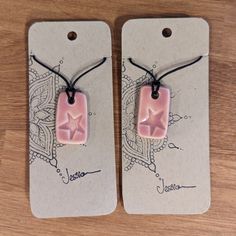 pair of pink ceramic earrings with black cord on wooden table next to white tag hanging from string