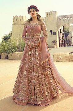 a woman standing in front of a castle wearing a pink and gold gown with long sleeves