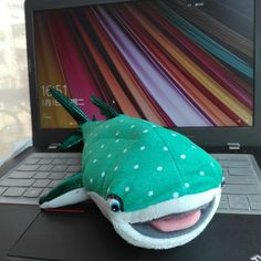 a green stuffed animal sitting on top of a laptop computer next to a mouse and keyboard