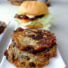 three burgers on white plates with lettuce and tomato in the back ground