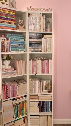 a bookshelf filled with lots of books next to a pink wall in a room