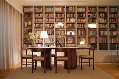 a dining room table surrounded by bookshelves with lamps on top and chairs around it