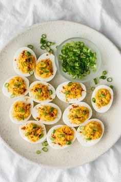 deviled eggs on a white plate with green onions and seasoning next to it