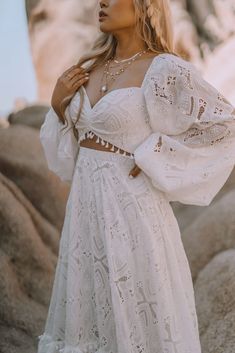 a woman in a white dress standing on rocks with her arms around her neck and hands behind her back