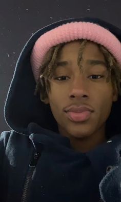 a young man with dreadlocks wearing a pink hat and hoodie looking at the camera