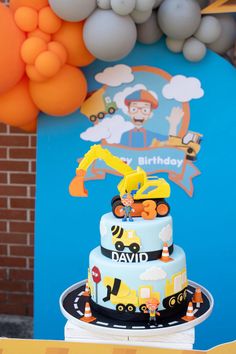 a birthday cake with construction themed decorations on the side and balloons in the air behind it