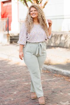 a woman standing on a brick road with her hands in her pockets and smiling at the camera