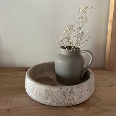 a gray vase with flowers in it sitting on a wooden table next to a white wall