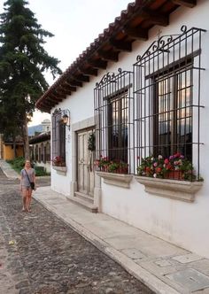 a woman is walking down the street in front of a building with flowers on it