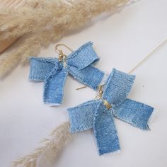 two pairs of blue bow earrings on a white surface next to some feathery material