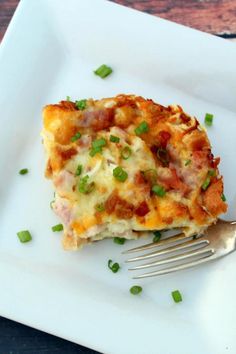 a piece of pizza on a white plate with a fork and some scallions