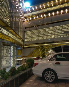 a white car parked in front of a building with lights hanging from it's ceiling