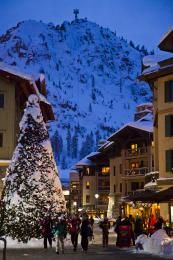 people are walking around in the snow near buildings and a christmas tree with lights on it