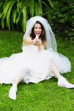 a woman in a wedding dress is sitting on the grass and pointing her finger at the camera